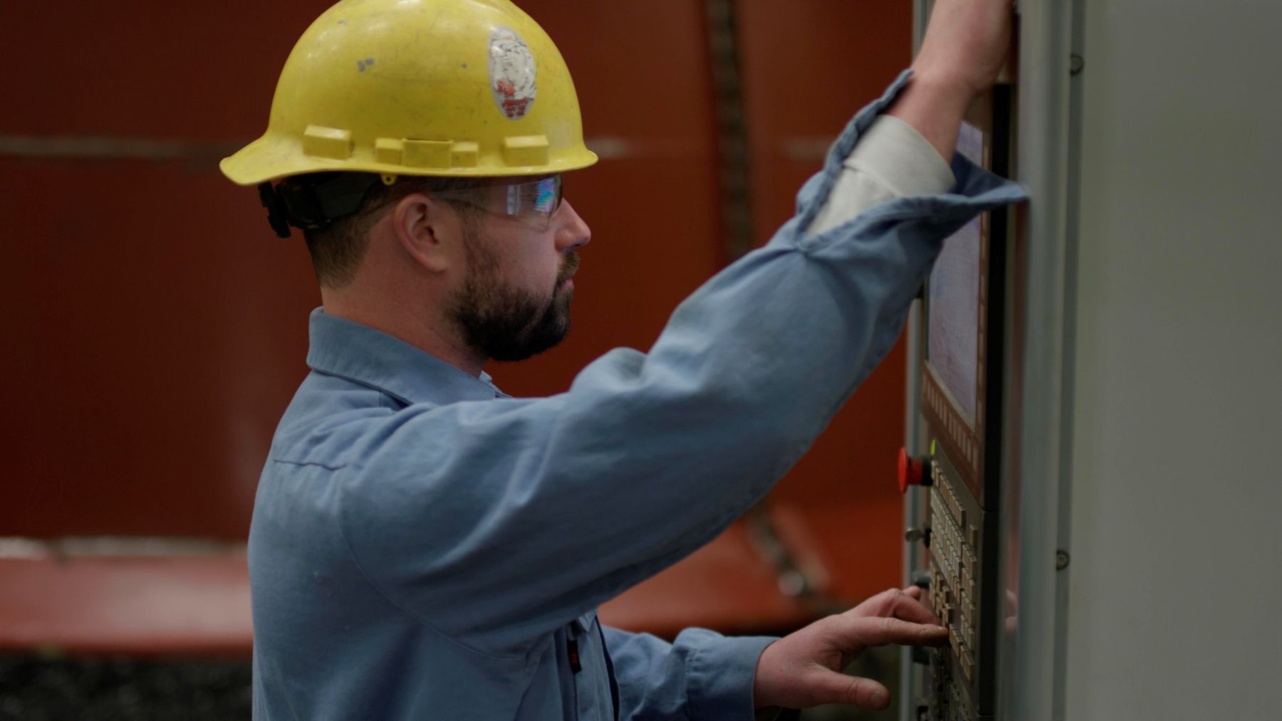 Brilex technician in a hard hat and safety glasses operating an industrial control panel